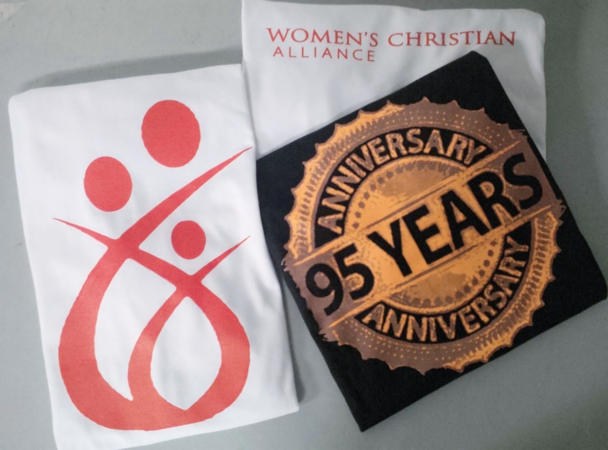 Light and dark apparel shows Women’s Christian Alliance branding alongside a gold-and-black “95 Years” anniversary design.